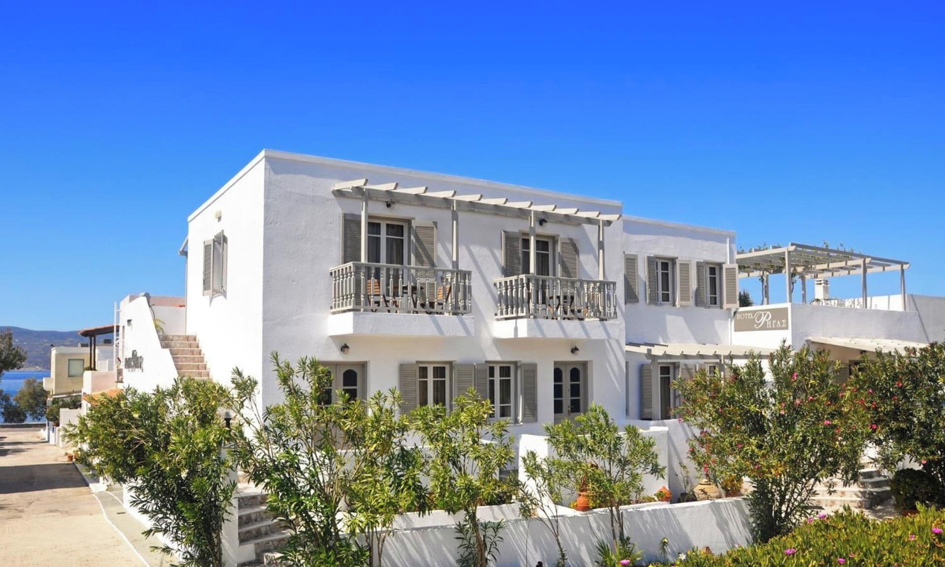 A white two-story hotel with balconies and a clear blue sky.
