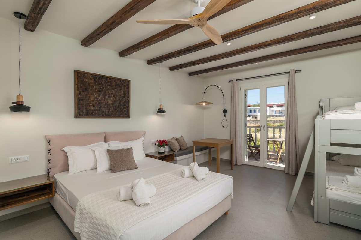 A bedroom with a large bed, a wooden ceiling, a small table, and a balcony with a view.