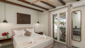A bedroom with a bed, bedside tables, a ceiling fan, a wall-mounted artwork, and a sliding glass door leading to an outdoor area. - Hotel Rigas (Milos)