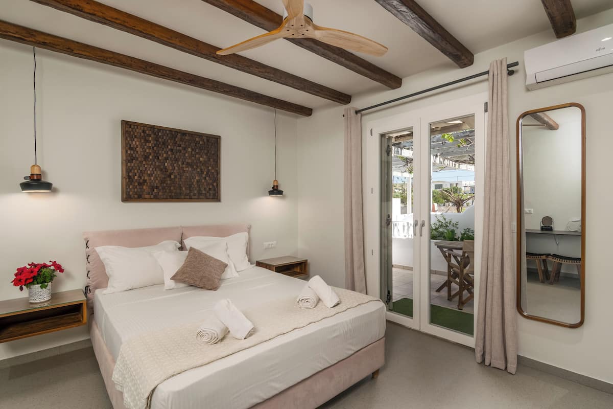 A bedroom with a bed, bedside tables, a ceiling fan, a wall-mounted artwork, and a sliding glass door leading to an outdoor area.