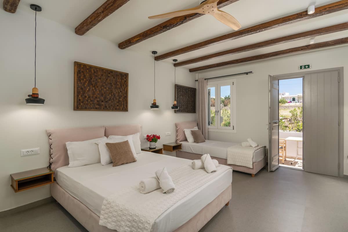 A bedroom with two beds, wooden beams, pendant lights, and a view through a door.