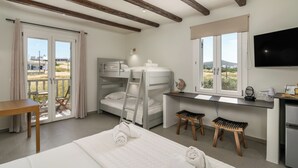 A bedroom with a bunk bed, a desk, a TV, and a balcony with a table and chairs. - Hotel Rigas (Milos)