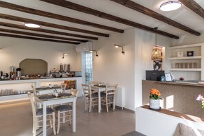 A modern kitchen with wooden beams, a dining area with white furniture, and a reception desk with a vase of flowers. - Hotel Rigas (Milos)