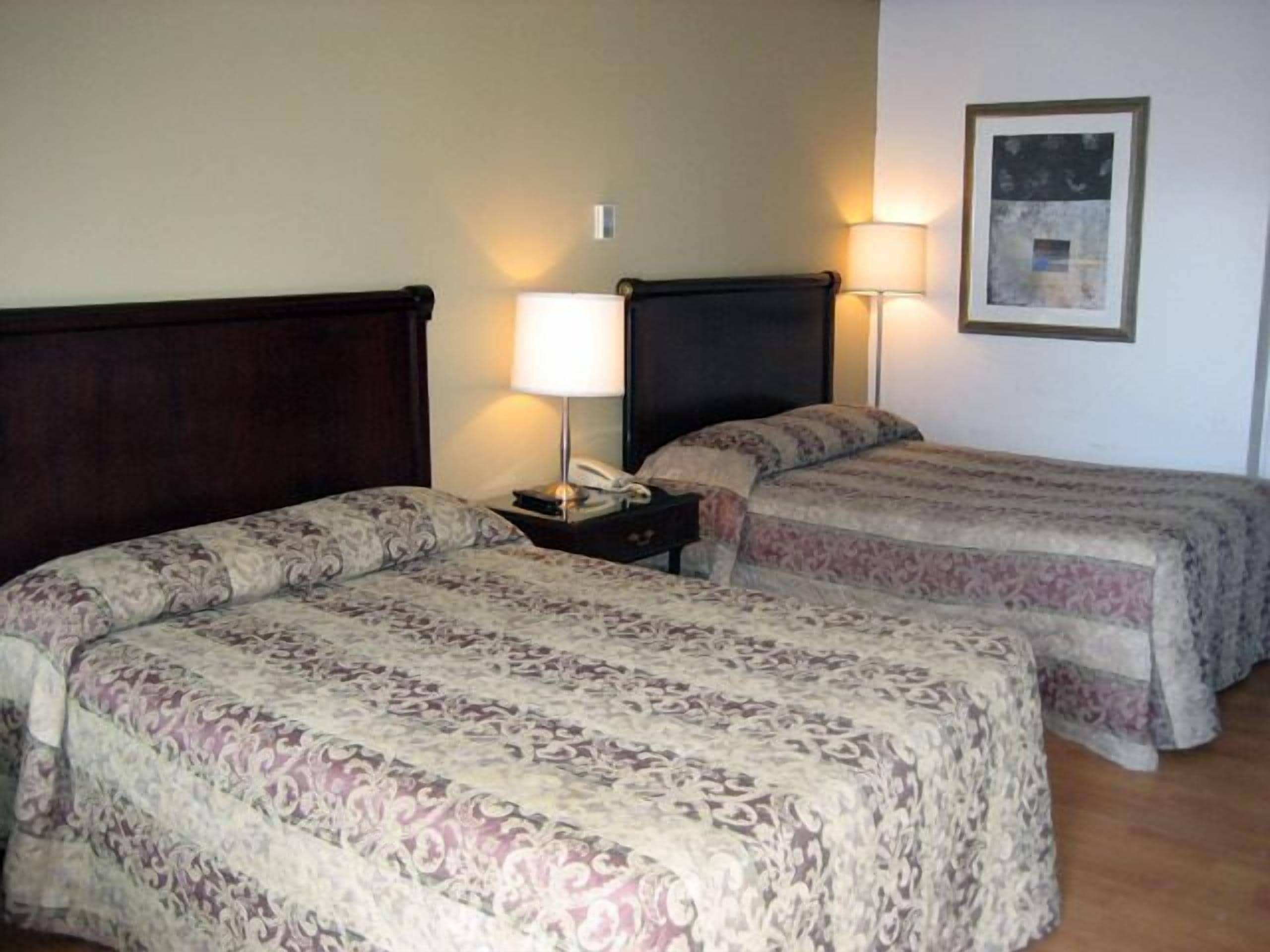 A hotel room with two beds, each with a patterned bedspread, bedside lamps, and a framed picture on the wall.