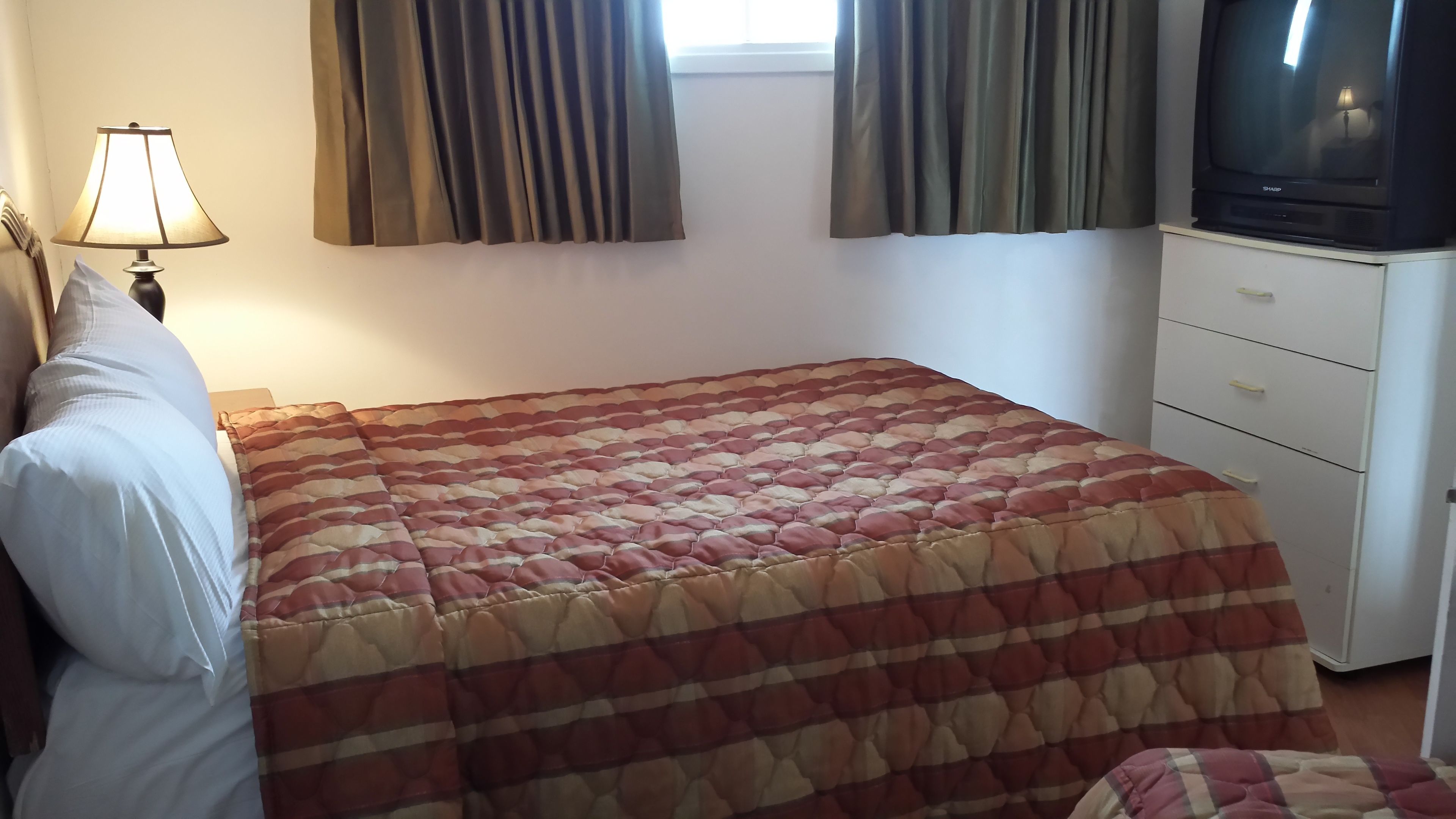 A bedroom with a bed, a TV, a lamp, and a window with curtains.