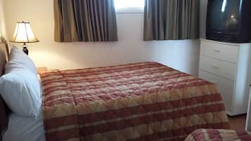 A bedroom with a bed, a TV, a lamp, and a window with curtains.