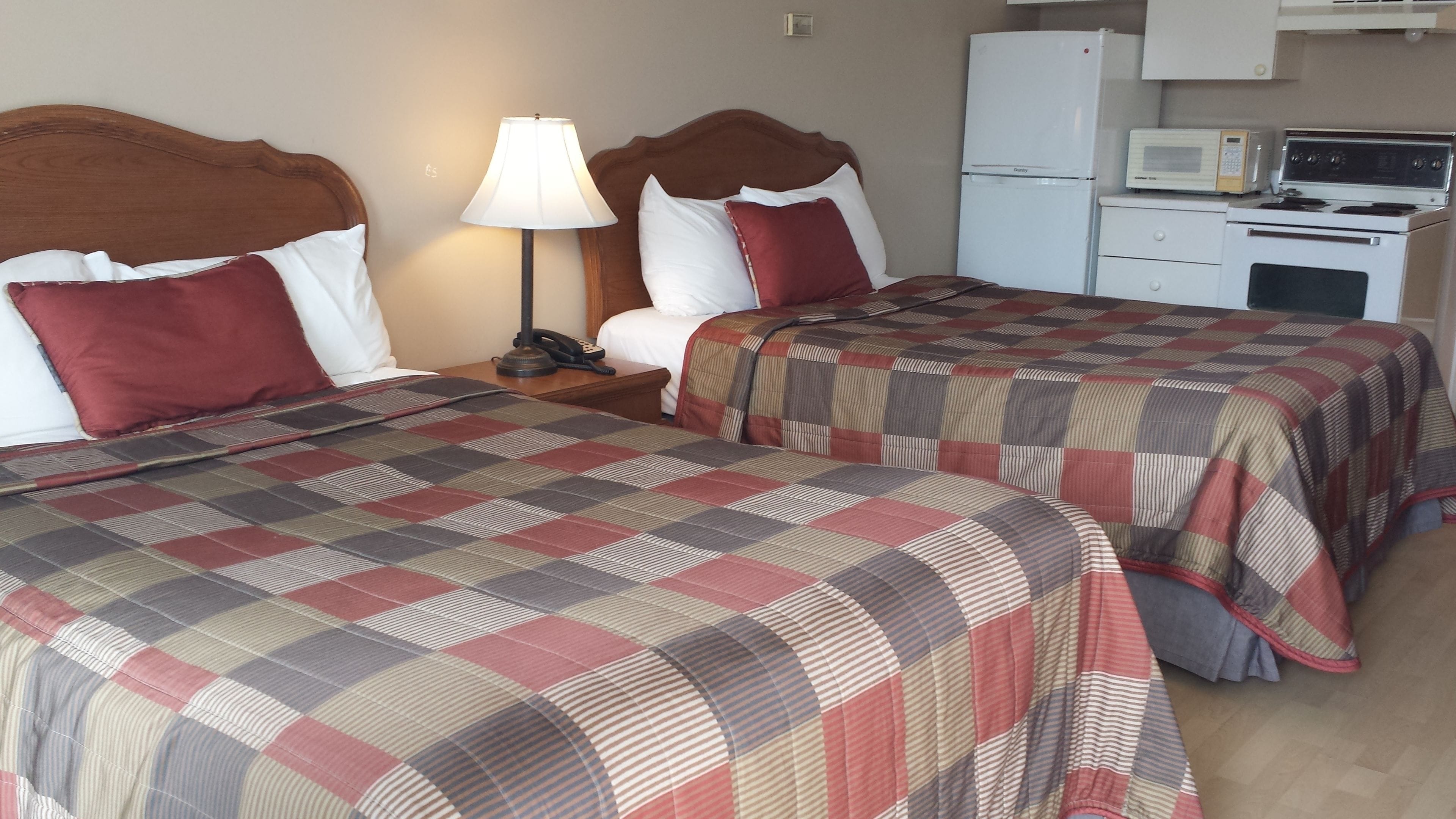 Ein Hotelzimmer mit zwei Betten, einem Nachttisch mit Lampe, einer Mikrowelle und einem Kühlschrank.