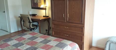 Un dormitorio con cama, escritorio, silla y armario.