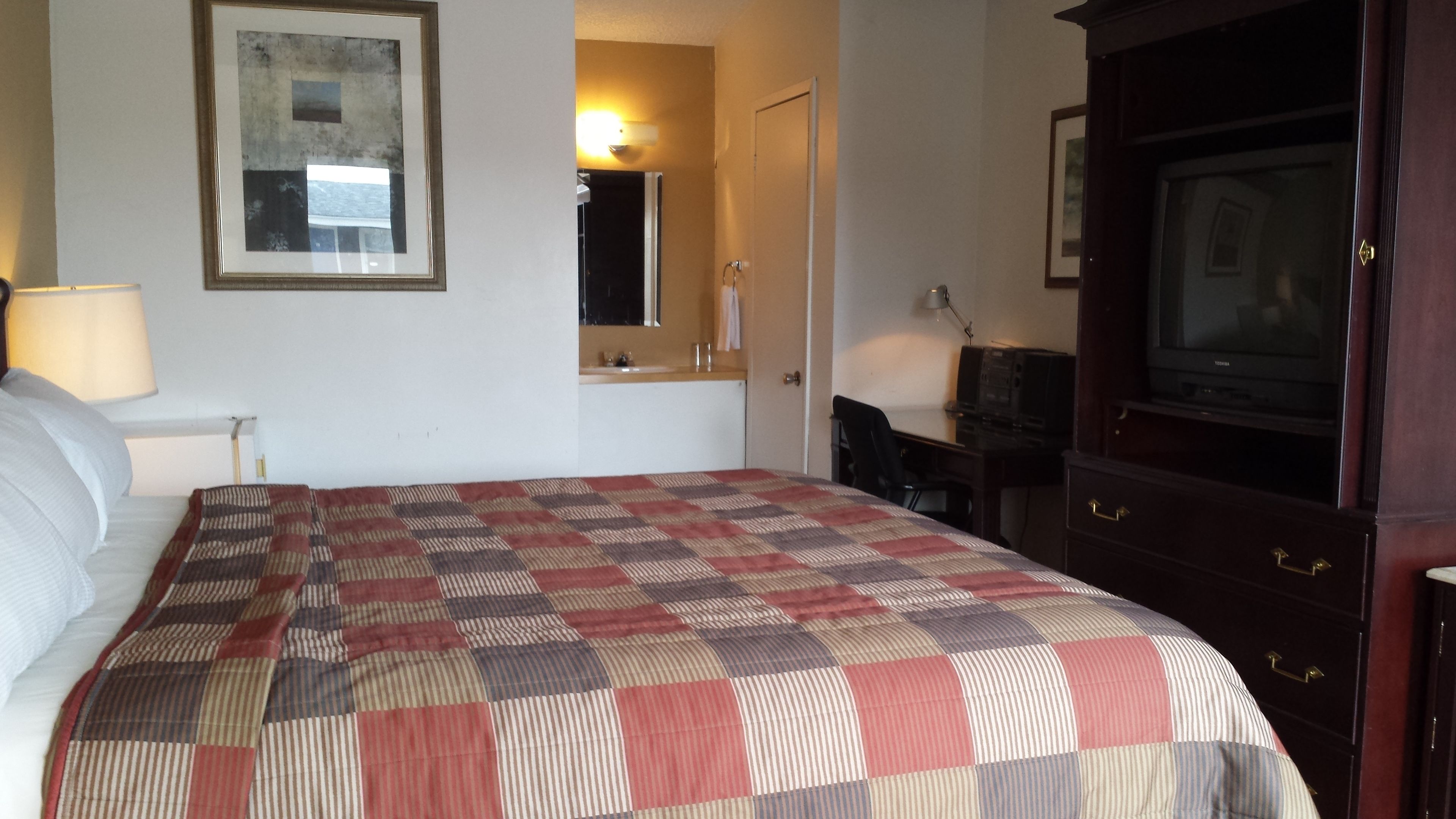A hotel room with a bed, a desk, a television, and a framed picture on the wall.