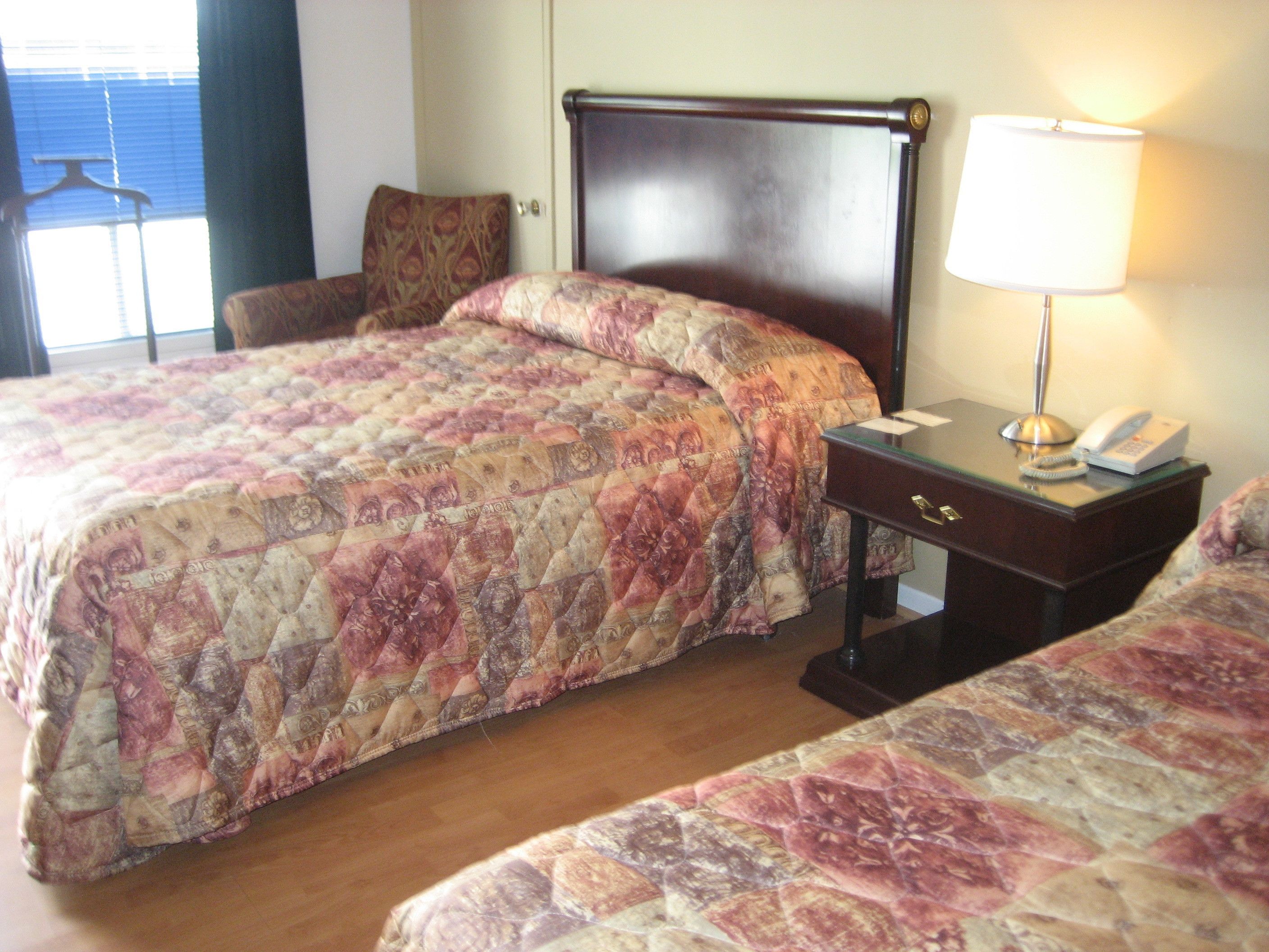 A hotel room with a large bed, a smaller bed, a nightstand with a lamp, and a chair.