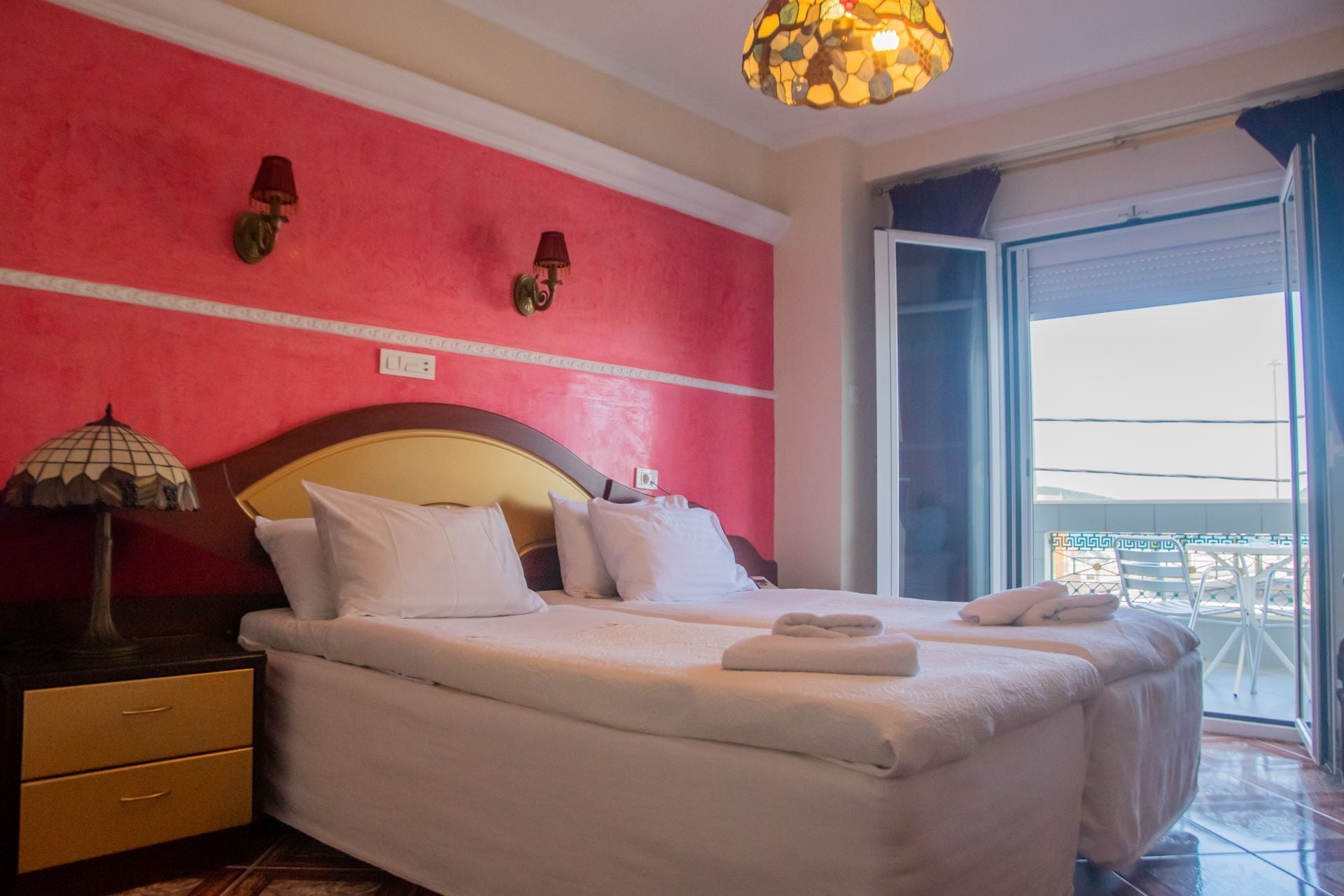 A hotel room with a bed, bedside tables, a lamp, and a view of the outside.