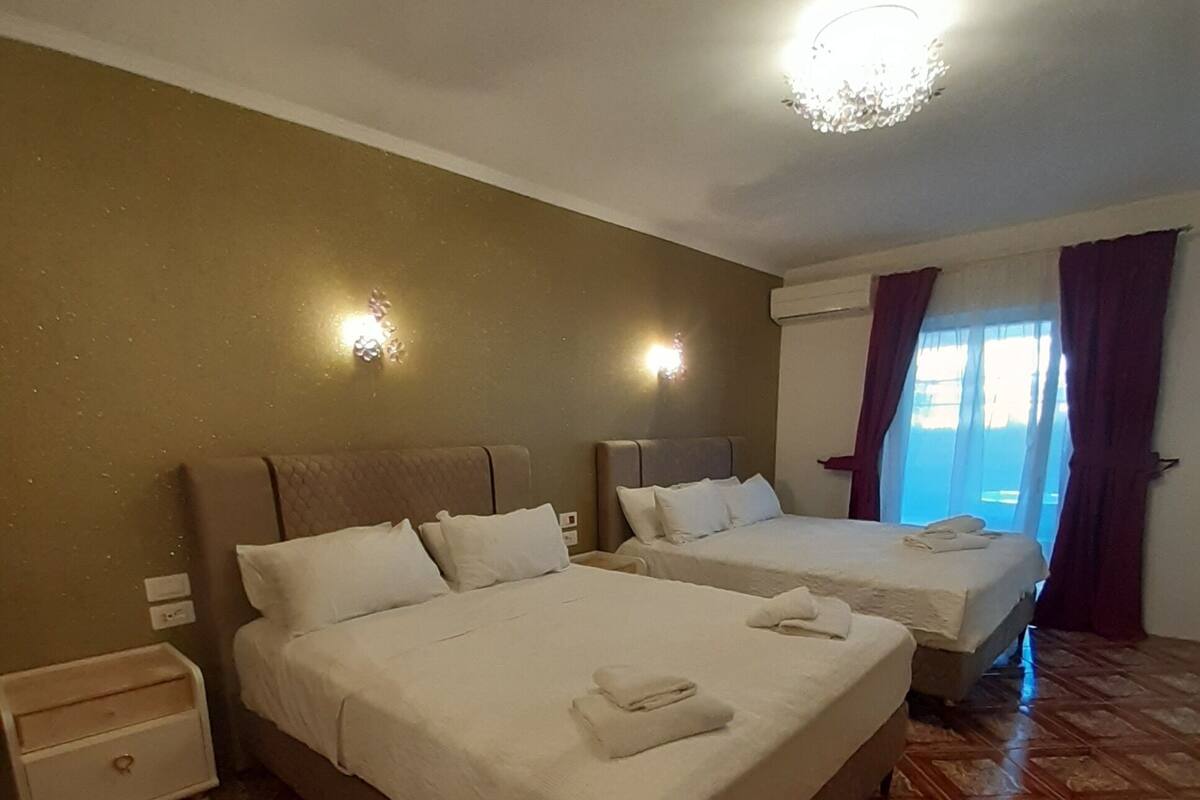 A hotel room with two beds, a nightstand, and a window with curtains.