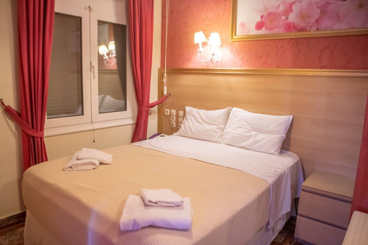 A hotel room with a bed, a nightstand, a lamp, and a window with curtains.
