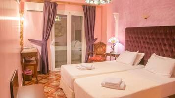 A hotel room with two beds, a sitting area with a chair and table, a decorative lamp, and a view through a glass door.