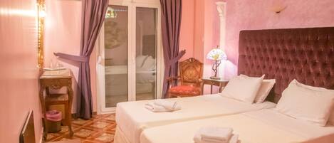 A hotel room with two beds, a sitting area with a chair and table, a decorative lamp, and a view through a glass door.