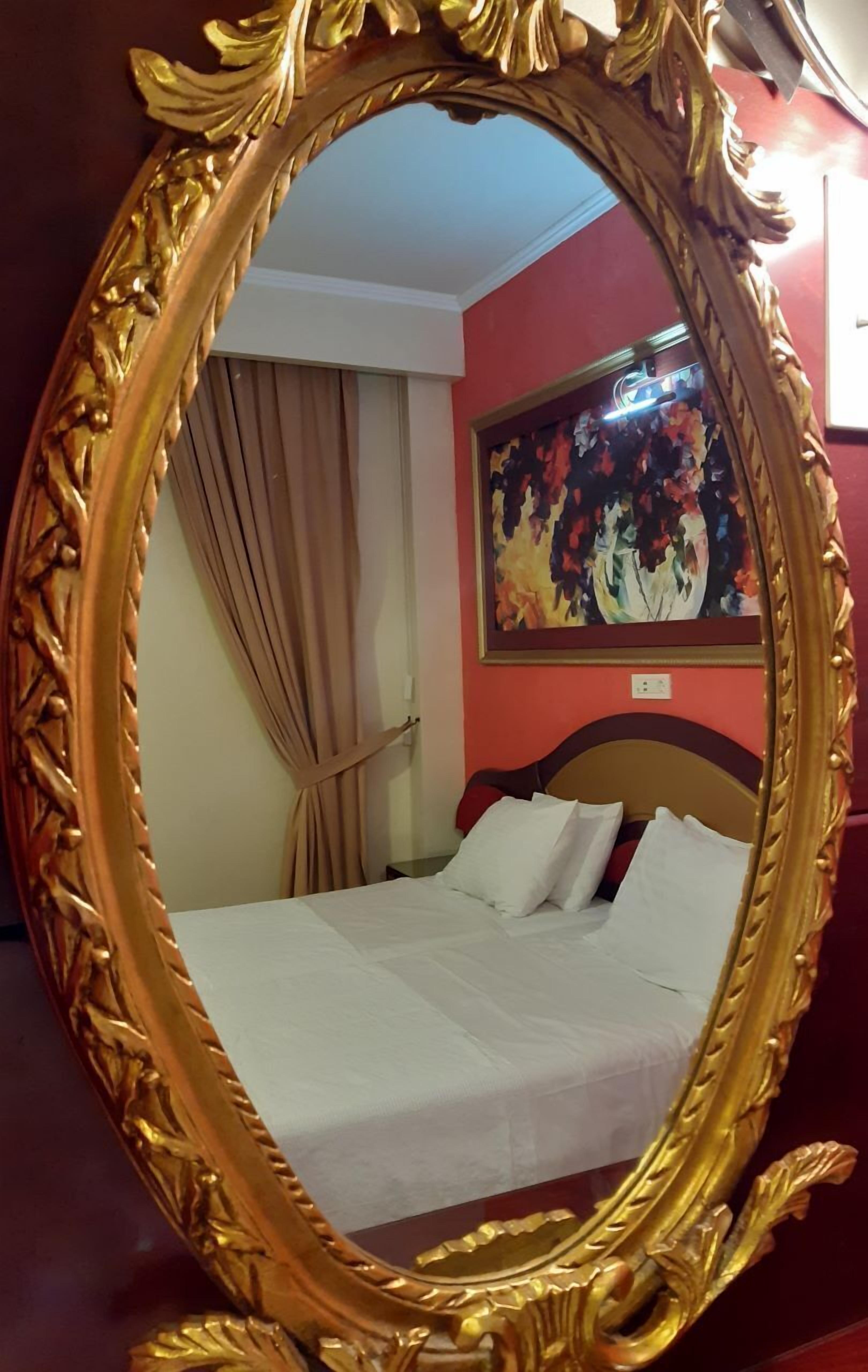 A room with a bed, a large ornate mirror, and a painting on the wall.
