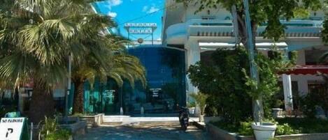 Entrada de un hotel con una palmera, un cartel de 'NO PARKING' y un edificio de fachada azul.