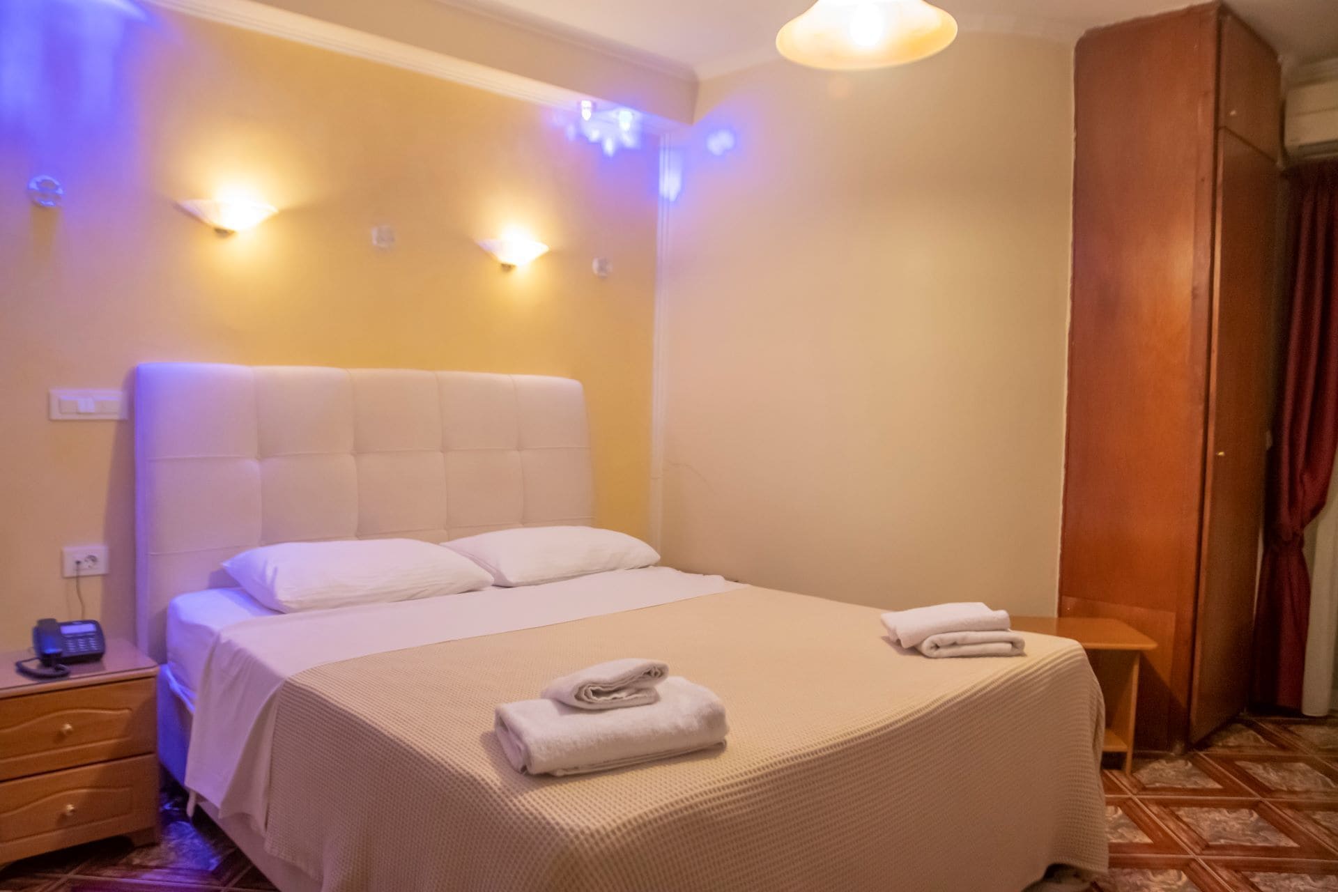 A hotel room with a large bed, bedside tables, a wardrobe, and wall-mounted lights.