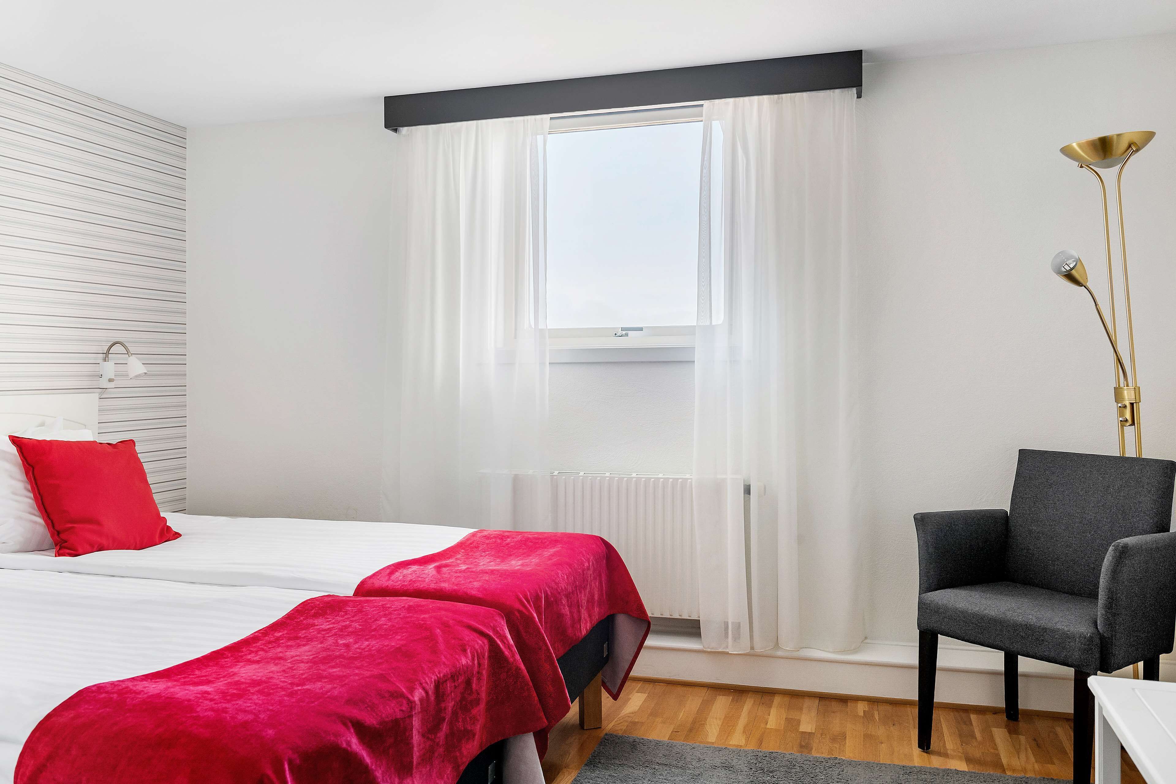 A hotel room with two beds, a chair, a floor lamp, and a window with curtains.