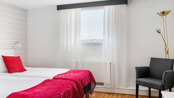 A hotel room with two beds, a chair, a floor lamp, and a window with curtains.