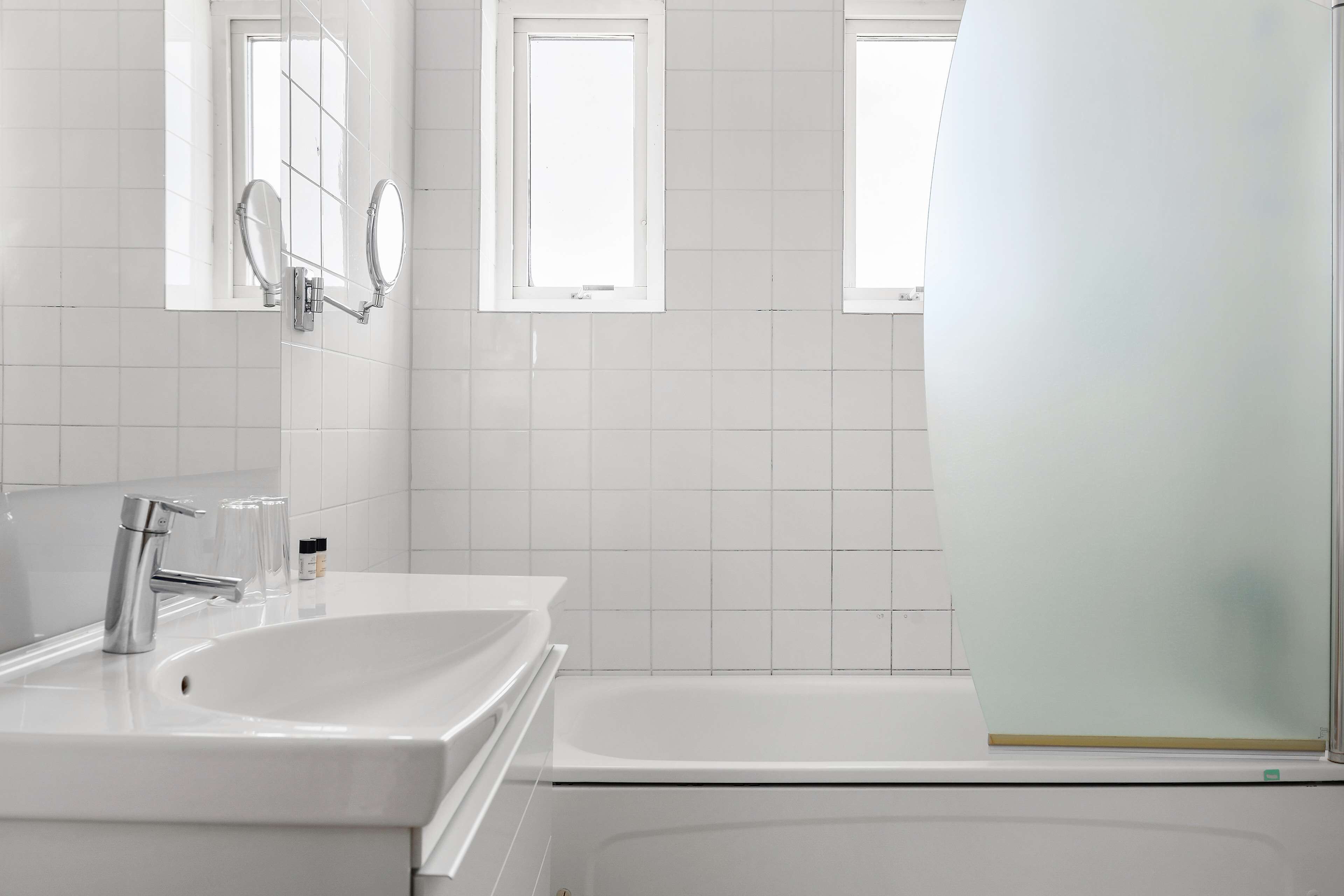 A modern bathroom with a white sink, a bathtub, and two mirrors.