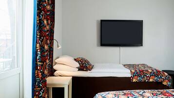 A hotel room with a bed, a TV mounted on the wall, a window with curtains, and a bedside table.