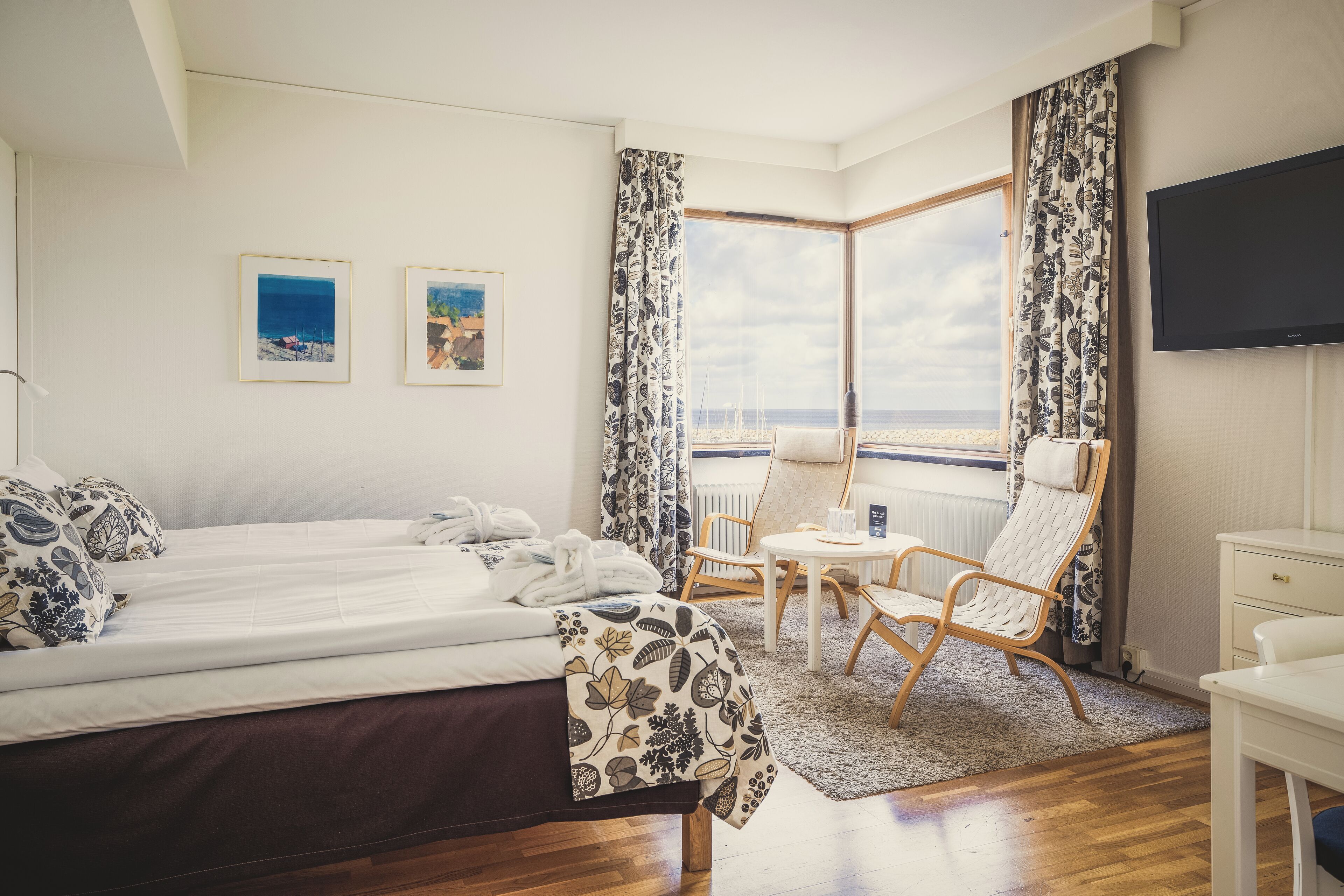 Hotellihuone, jossa on suuri sänky, tuoli, pieni pöytä ja televisio.