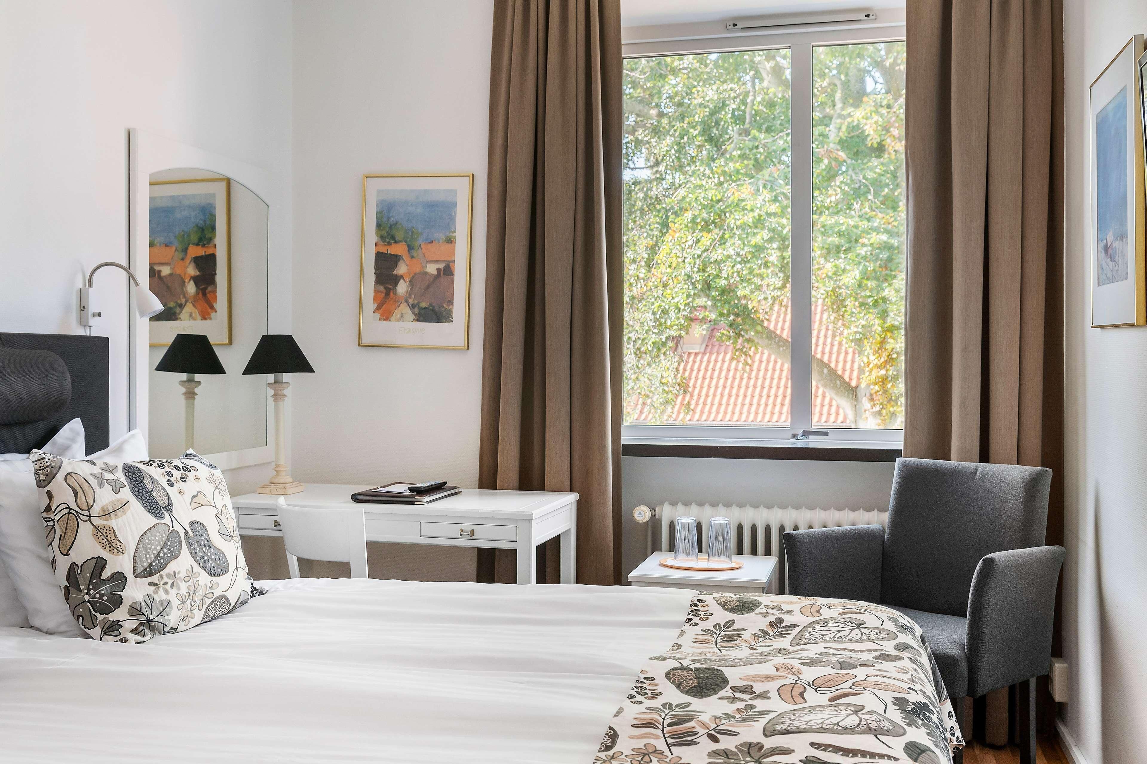 A hotel room with a bed, a desk, a chair, and a window with curtains.