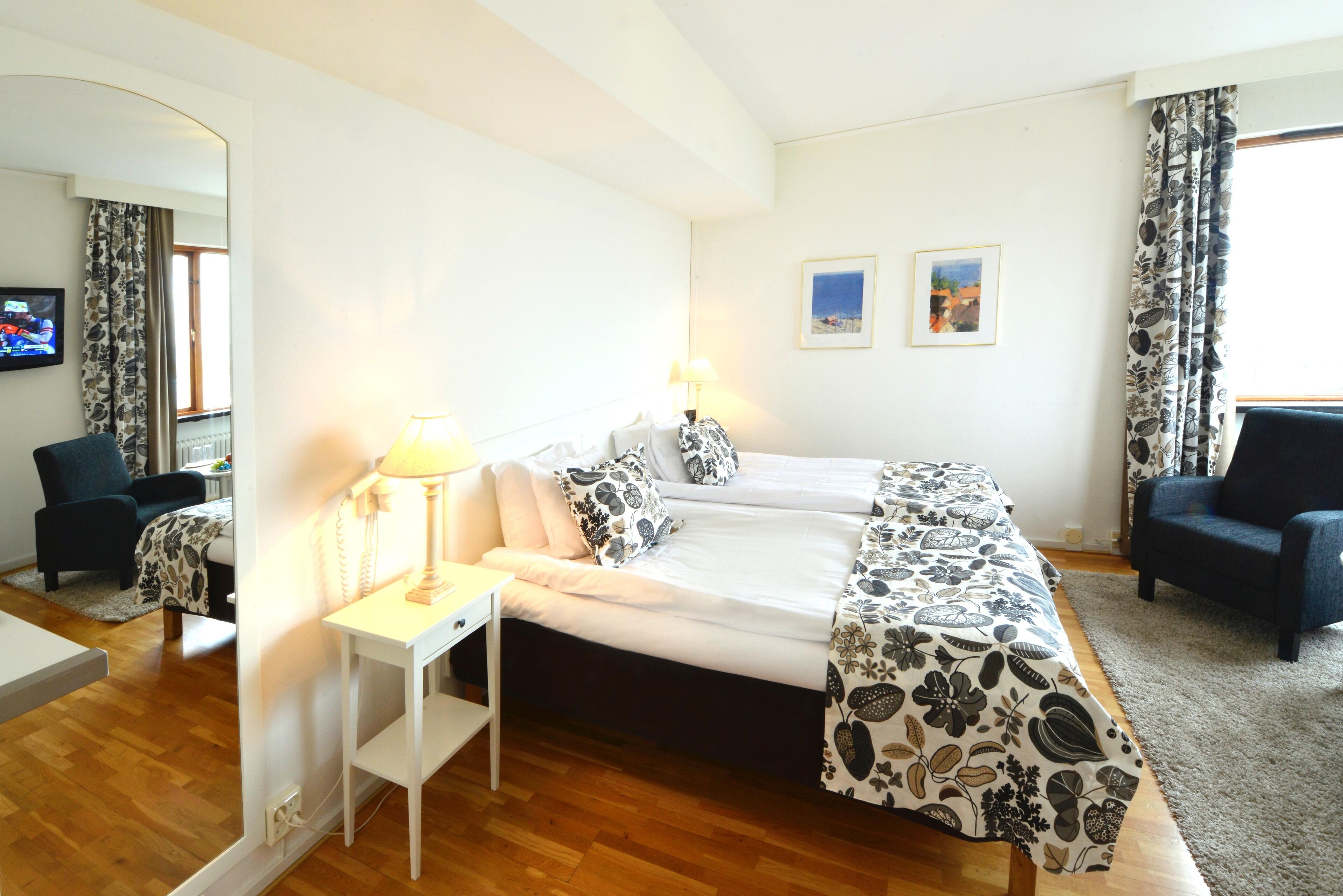 Una habitación de hotel con una cama, dos mesitas de noche, una silla, un escritorio y un espejo.