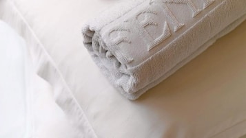 A neatly folded white towel with a subtle pattern, placed on a bed with white pillows.