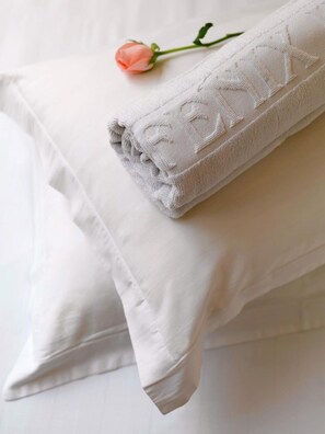 A neatly folded white towel with a subtle pattern, placed on a bed with white pillows.