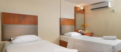 Habitación de hotel con dos camas individuales, cabecero de madera, mesita de noche con lámpara, espejo y aire acondicionado.