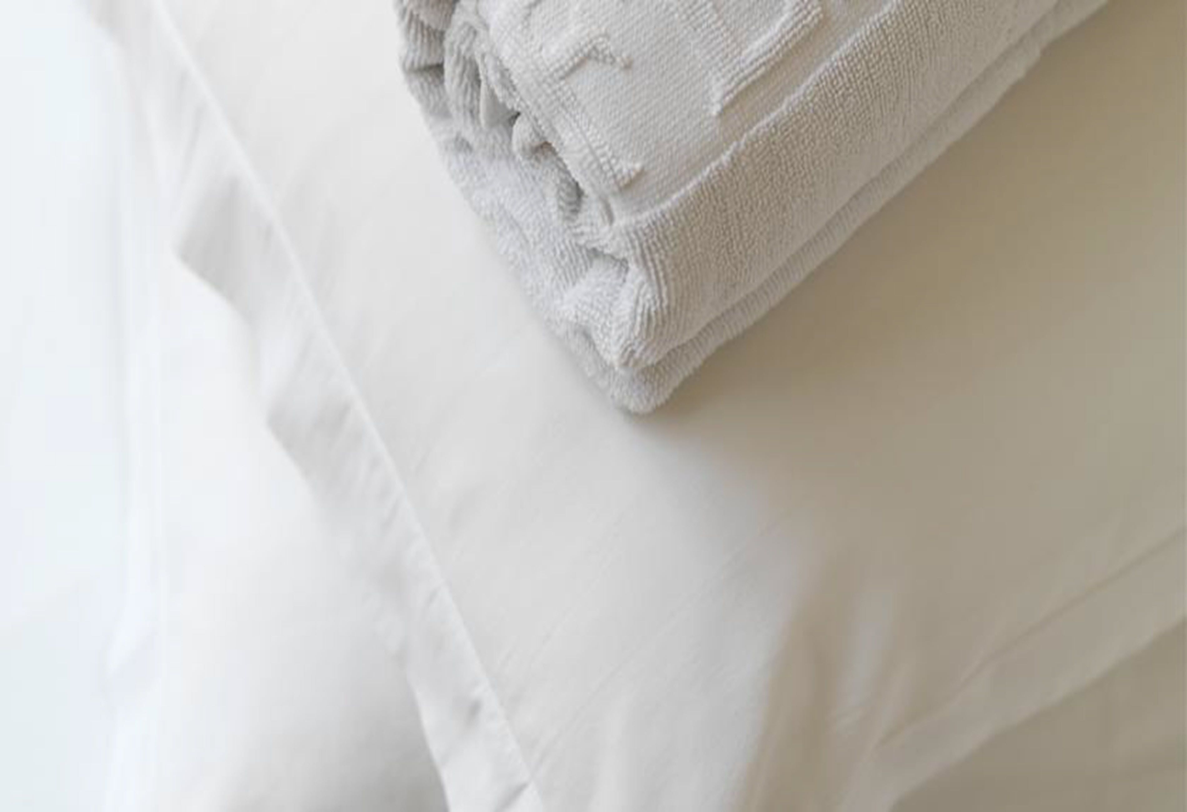Une serviette blanche, soigneusement pliée, est posée sur un lit blanc.
