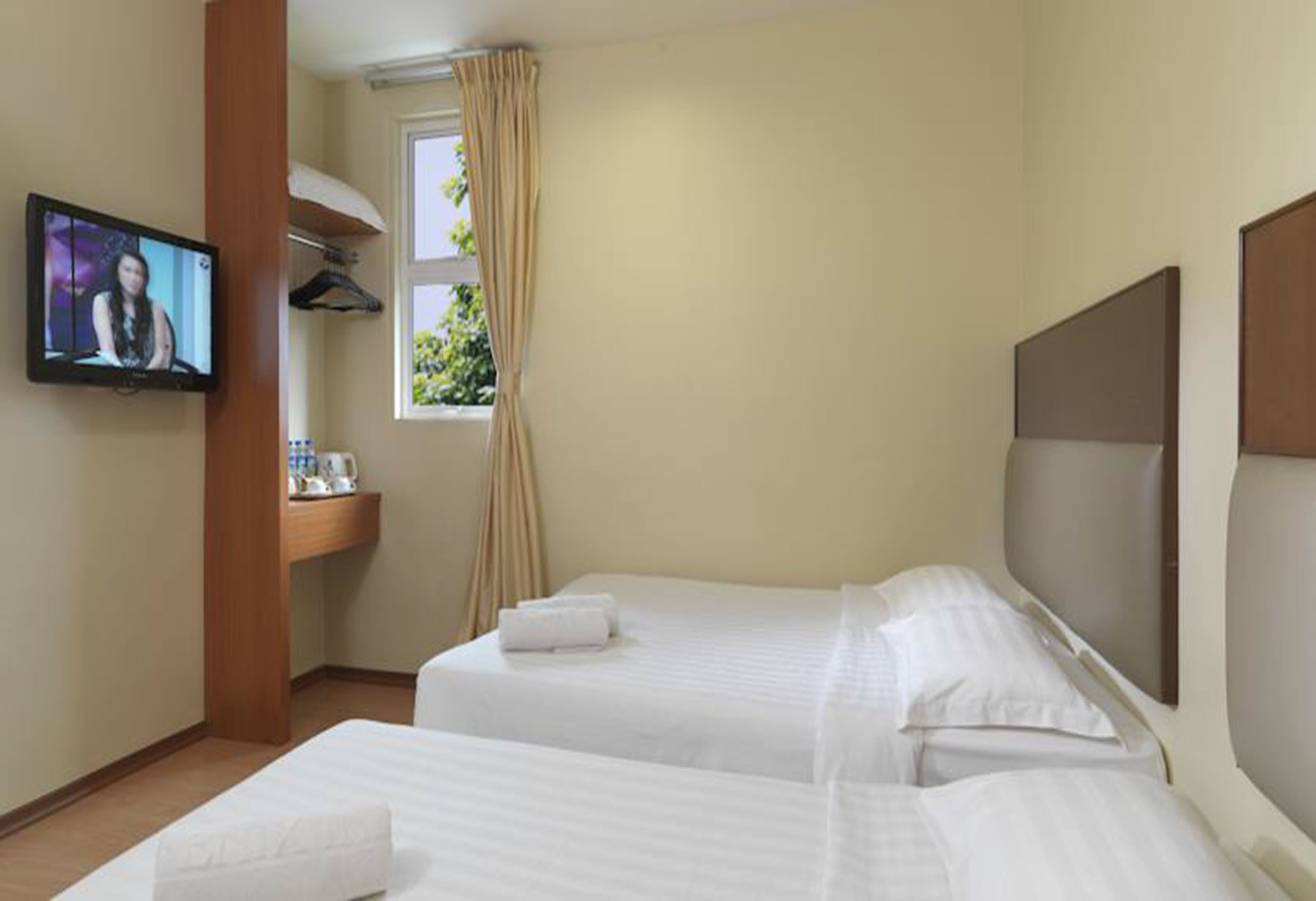 A hotel room with two beds, a TV, a window with curtains, and a wooden desk with a cup and saucer.