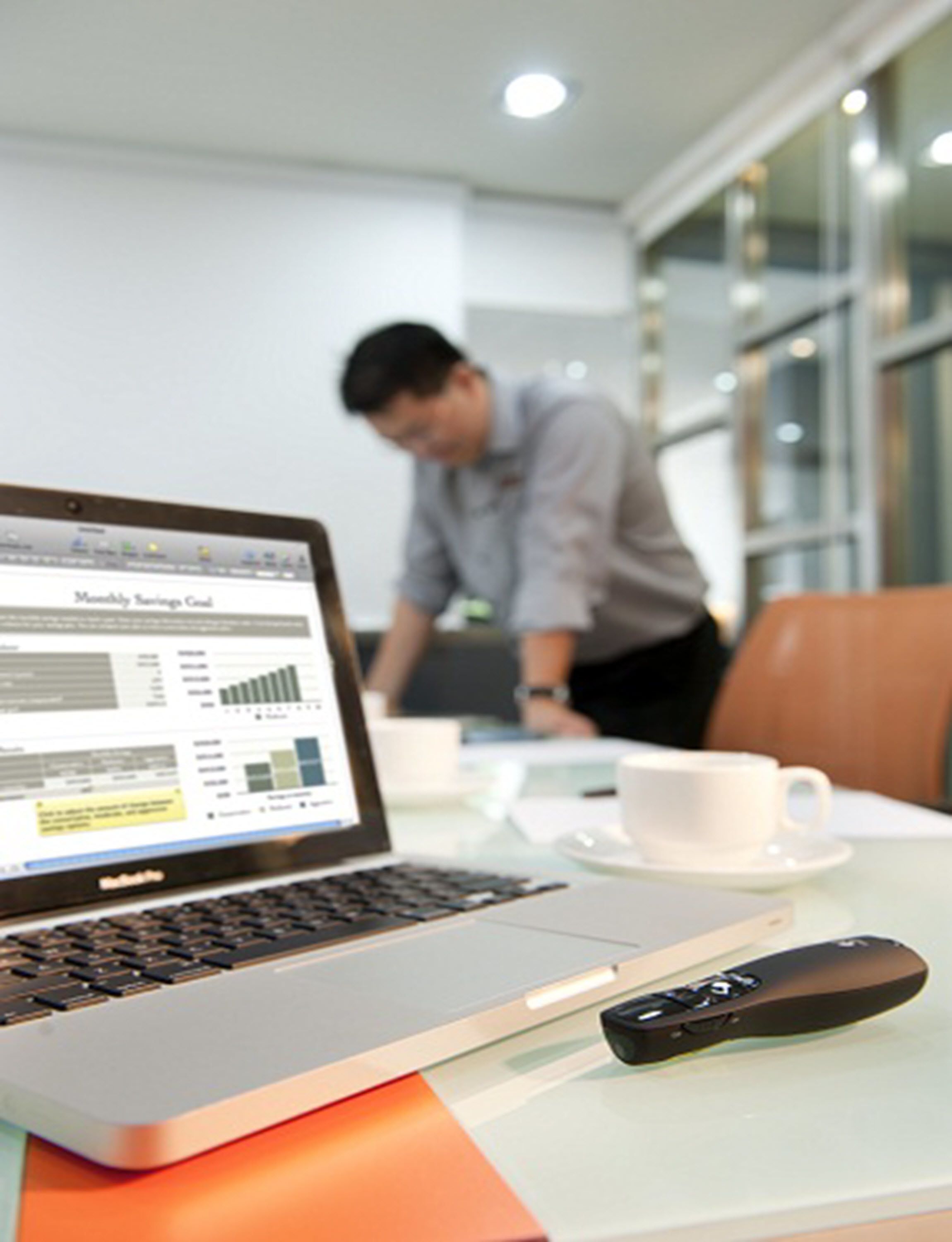 Un ordinateur portable affichant un rapport financier, une télécommande et une tasse blanche posés sur une table dans un bureau moderne.