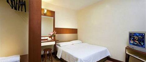 A hotel room with a bed, a desk with a chair, a mirror, and a television.