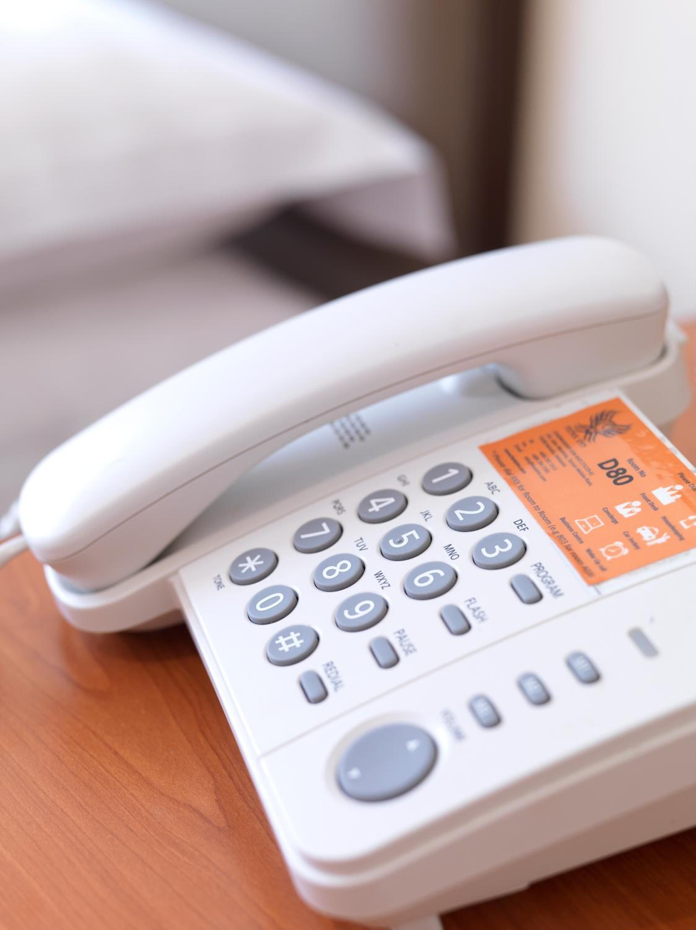 A white telephone with a numeric keypad and a few function buttons, placed on a wooden surface.