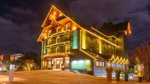A hotel with a green facade, multiple balconies, and a lit entrance. - Hotel Laghetto Viale (Gramado)