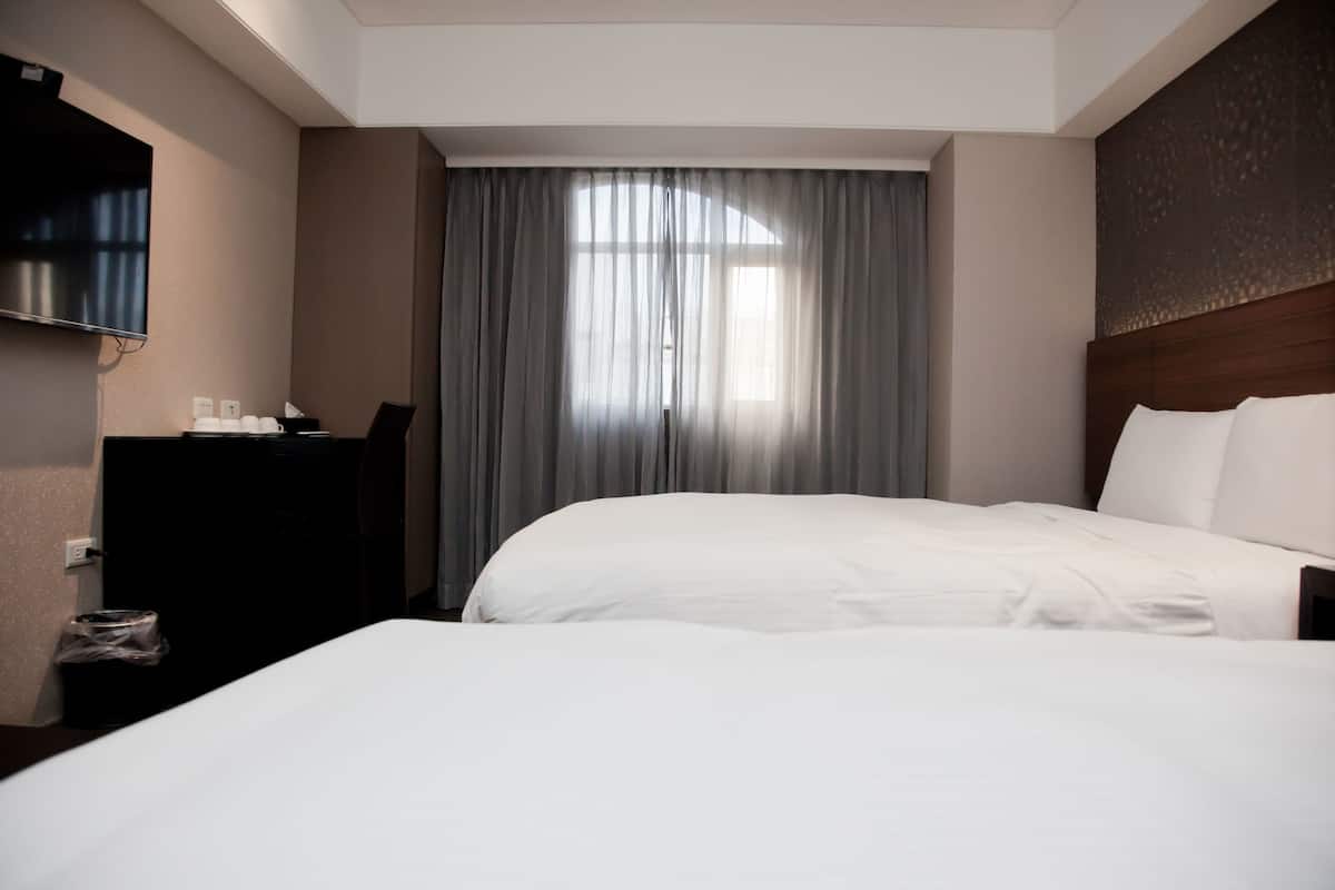 A hotel room with a large bed, a desk with a chair, a television mounted on the wall, and a window with curtains.
