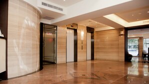 A modern lobby with a curved wall, a reception desk, and three elevators. - KDM Hotel (Taipei)