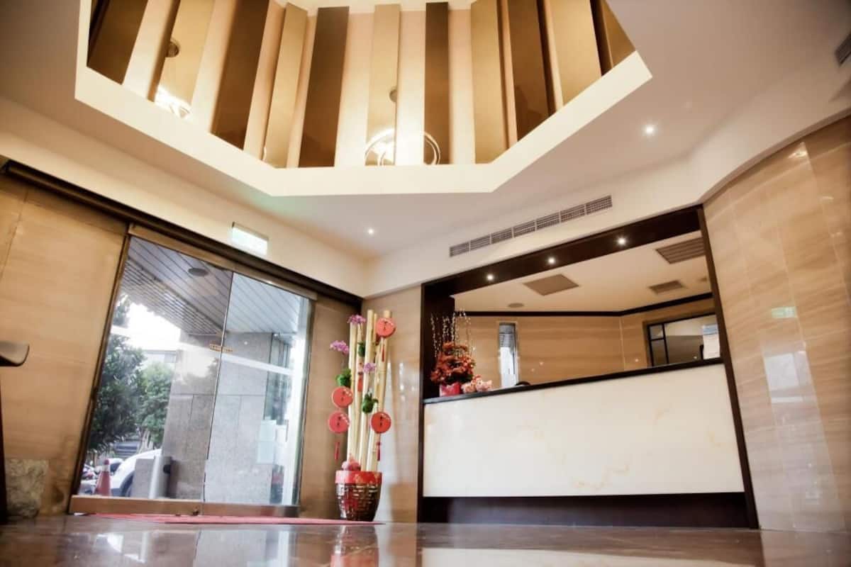 A modern hotel lobby with a reception desk, large windows, and a decorative plant arrangement.