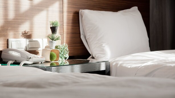 A neatly made hotel room with a bed, a bedside table with a phone, a lamp, and a small potted plant. - KDM Hotel (Taipei)