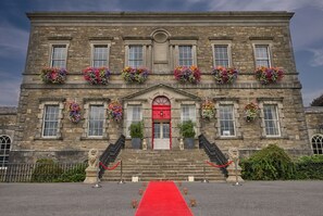 A historic stone building with a red carpet leading to the entrance, adorned with flower boxes and statues.
