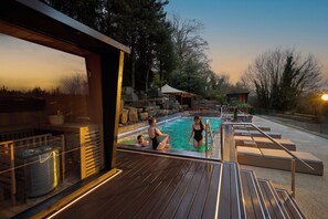 An outdoor swimming pool with wooden deck, lounge chairs, and a stone wall.