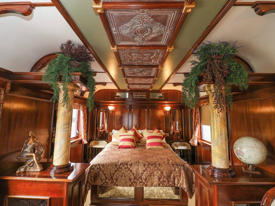Un dormitorio lujoso con una cama grande, techo ornamentado y columnas decorativas.