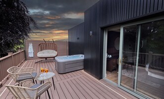 Una terraza con sillas de mimbre, un jacuzzi y una puerta de vidrio que da a un espacio interior.