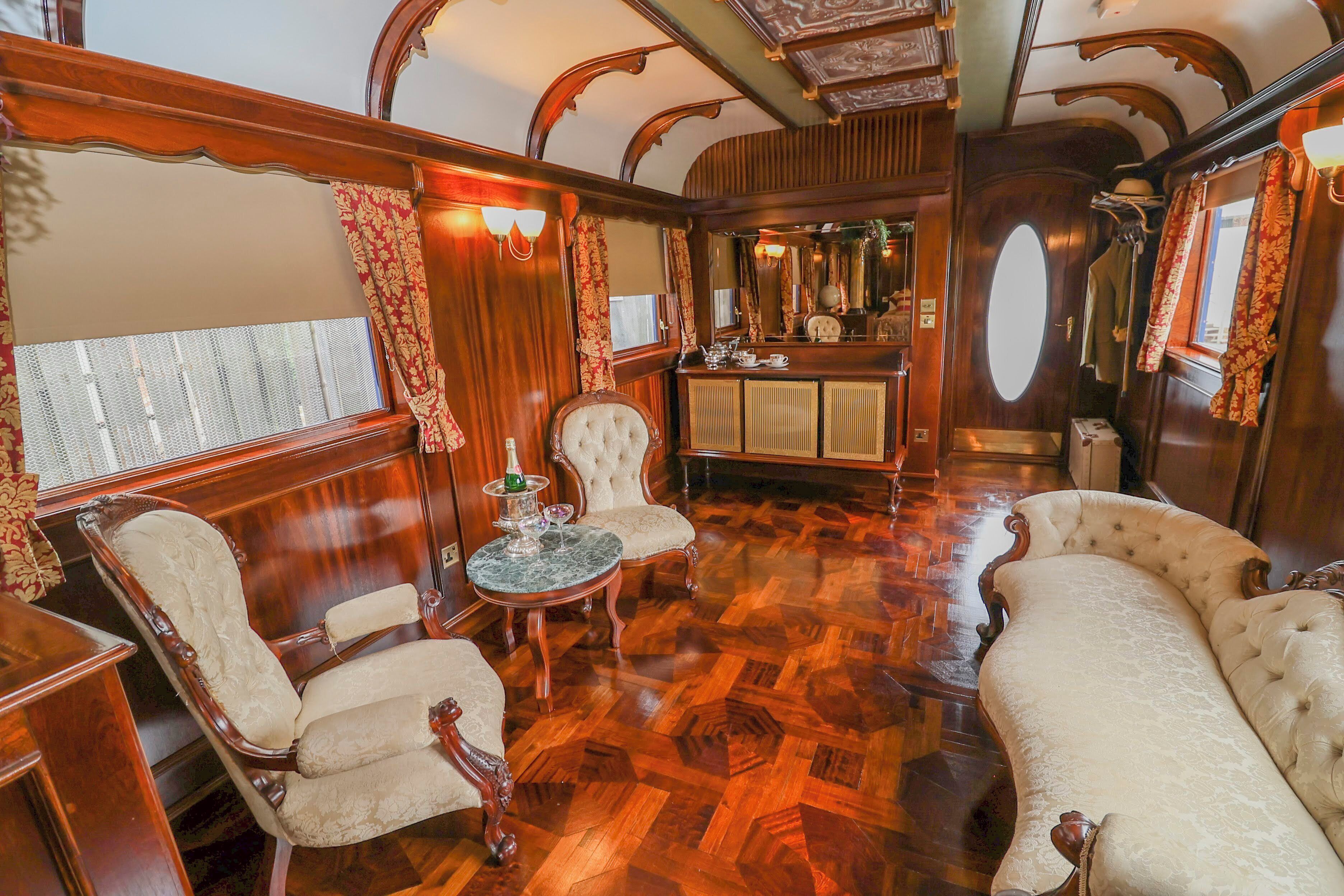 Un lujoso vagón de tren con paneles de madera ornamentados, asientos mullidos y una pequeña zona de bar.