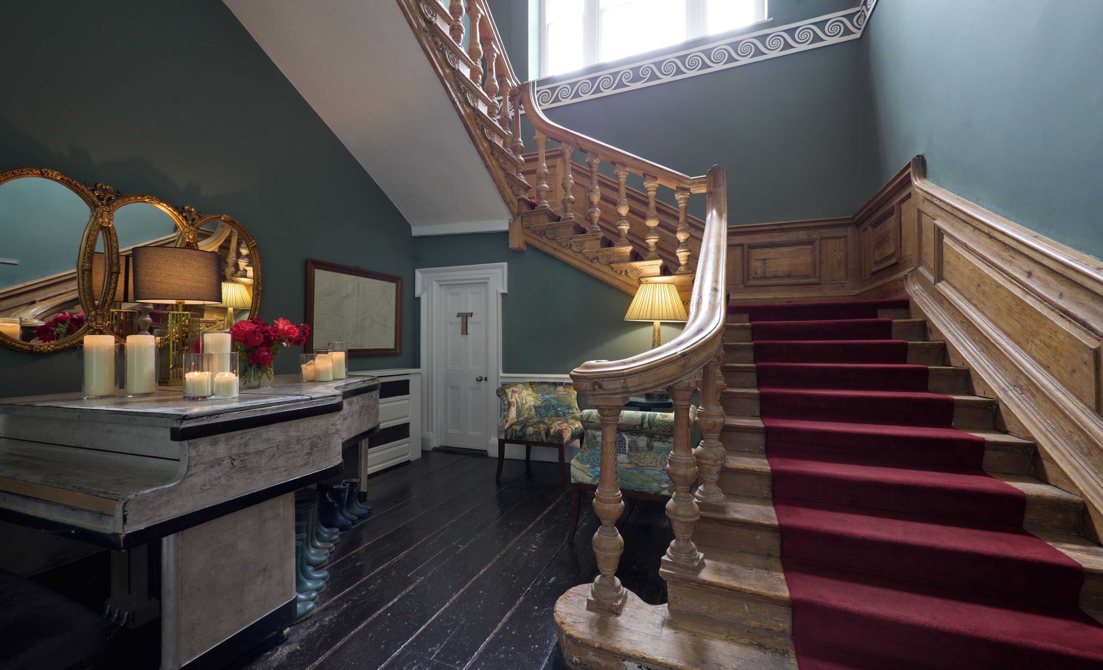 A grand staircase with a red carpet, a wooden railing, and a chandelier.
