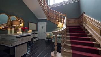 A grand staircase with a red carpet, a wooden railing, and a chandelier.