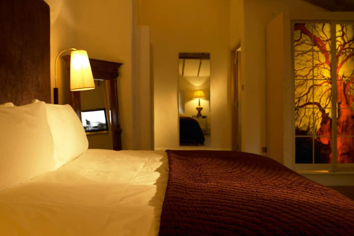 A hotel room with a bed, a desk, a chair, and a window with a tree view.